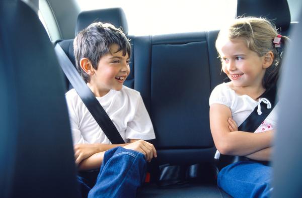 2 Kids wearing seat belts sitting in a car